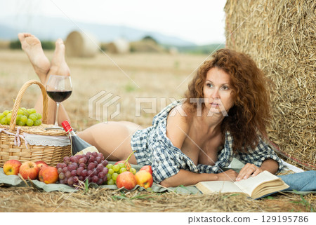 Woman in checkered shirt spends time in field, settled down in nature with book 129195786