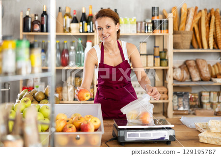 Adult woman seller weighs apples in bag 129195787