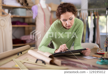 Woman tailor creates sketch of dress on tablet 129195812