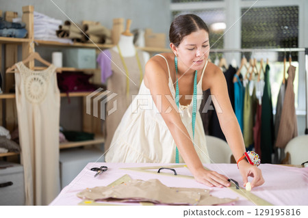 Using ruler, woman tailor draws dress diagram scheme on fabric 129195816
