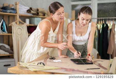 Two young female dressmakers drawing on tablet 129195829