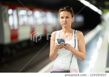 Adult woman stands at subway station with phone 129195837
