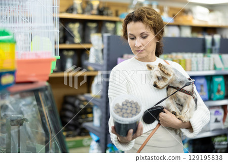 Buyers woman with Yorkshire Terrier choose healthy food and nutrition for pet in tin can 129195838