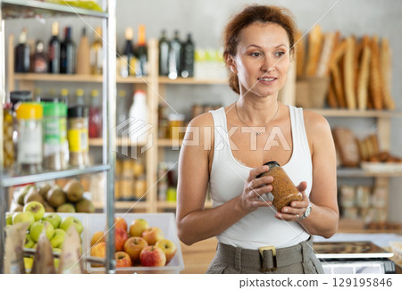Female customer carefully choosing can of lentils in grocery supermarket 129195846