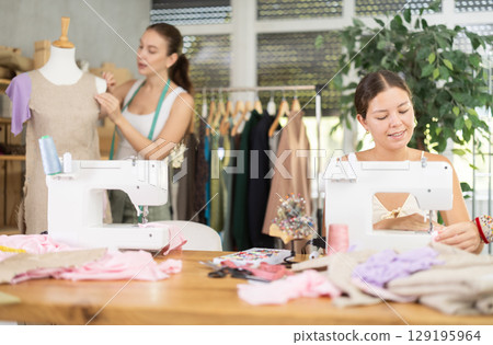 Woman seamstress operating by sewing machine. Assistant work with mannequin in background Woman seamstress operating by sewing machine. Assistant work with mannequin in background 129195964