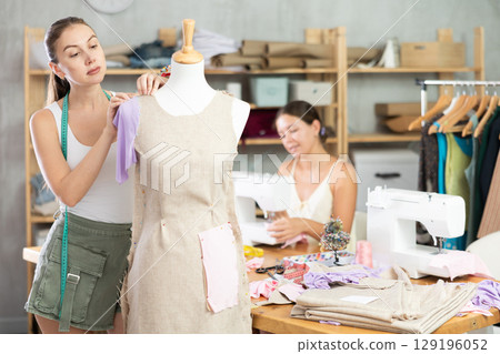 Tailor work with mannequin. Assistant sewing in background Tailor work with mannequin. Assistant sewing in background 129196052