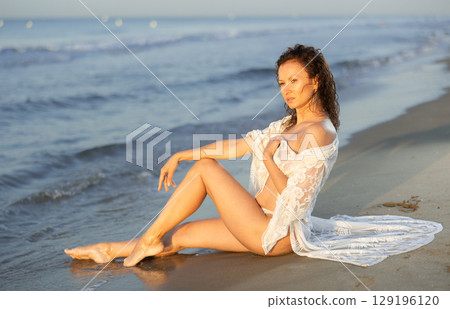 Adult woman in white peignoir sitting on coast 129196120