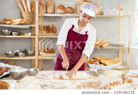 Skilled female baker slicing dough in artisan bakery Skilled female baker slicing dough in artisan bakery 129196138
