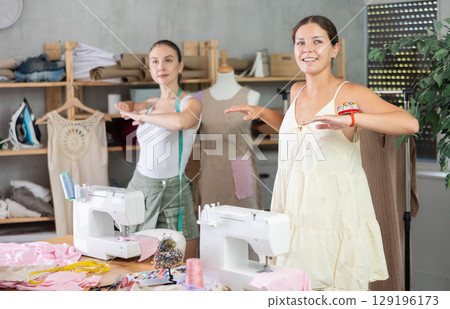 Female dressmakers doing a warm-up in the workshop in summer 129196173