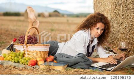 Woman settles down in nature with laptop, laying and performs creative work Woman settles down in nature with laptop, laying and performs creative work 129196176