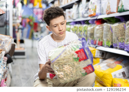 Teenager choosing straw bedding for cage of small pets in store Teenager choosing straw bedding for cage of small pets in store 129196234