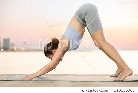 Near sea during sunset, girl performs Adho Mukha Svanasana 129196303