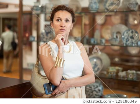 Woman with piece of paper and phone in hands walks around museum hall, view exhibition Woman with piece of paper and phone in hands walks around museum hall, view exhibition 129196349