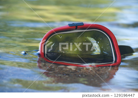 Snorkeling mask resting on the surface of a clear, shallow body of water. Snorkeling mask resting on the surface of a clear, shallow body of water. 129196447