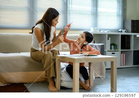 Happy mom assisting young girl with schoolwork at home Happy mom assisting young girl with schoolwork at home 129196597