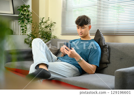 Relaxed caucasian male sitting on couch and using smartphone at home Relaxed caucasian male sitting on couch and using smartphone at home 129196601