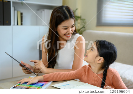 Asian mother with digital tablet guiding child during home study for creative learning Asian mother with digital tablet guiding child during home study for creative learning 129196604
