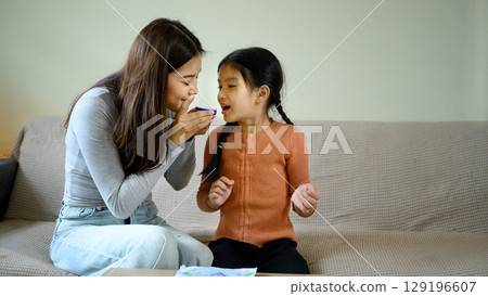 Happy mom and daughter enjoying a beauty care routine together in a living room Happy mom and daughter enjoying a beauty care routine together in a living room 129196607