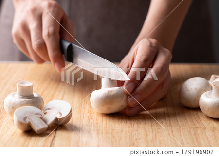 Hand holding kitchen knife and cutting white Button mushroom or Champignon mushroom on wooden board Hand holding kitchen knife and cutting white Button mushroom or Champignon mushroom on wooden board 129196902