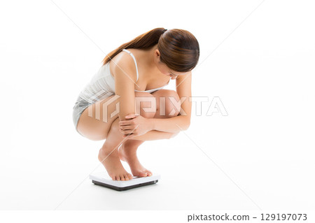 A young woman weighs herself on a bathroom scale. 129197073