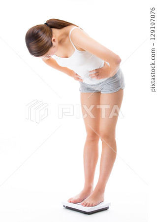 一名年輕女子在浴室體重計上稱體重。 129197076
