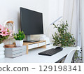 Minimalist home office setup with monitor, keyboard, headphones, books, and potted plants. 129198341