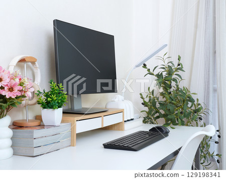 Minimalist home office setup with monitor, keyboard, headphones, books, and potted plants. 129198341