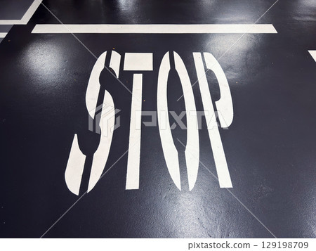 Bold white stop sign on dark asphalt surface in parking lot with clear lines 129198709