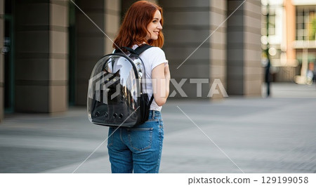 Stylish woman with her black cat in transparent backpack enjoys urban walk. 129199058