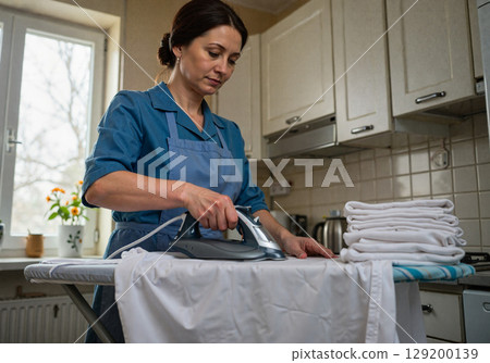 Woman ironing clothes in a cozy kitchen 129200139