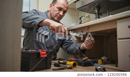 Man repairing sink under kitchen cabinet 129200566