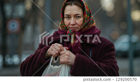 Woman with scarf looking serious while holding shopping bag Woman with scarf looking serious while holding shopping bag 129200570