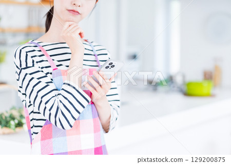 A housewife is searching on her smartphone, unable to decide what to cook. A housewife is searching on her smartphone, unable to decide what to cook. 129200875