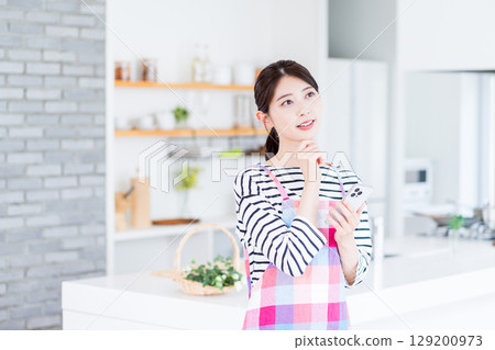 一位家庭主婦正在用智慧型手機搜索,不知道該做什麼菜。 一位家庭主婦正在用智慧型手機搜索,不知道該做什麼菜。 129200973