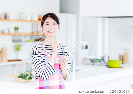 A housewife is searching on her smartphone, unable to decide what to cook. 129201023