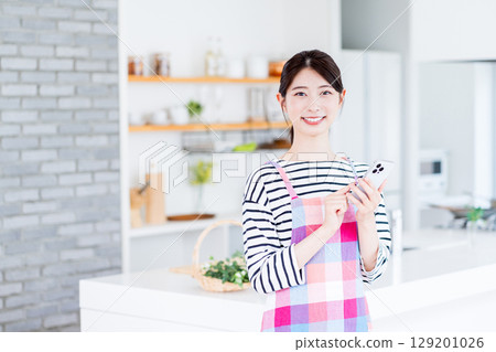 A housewife is searching on her smartphone, unable to decide what to cook. 129201026