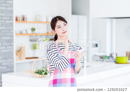 A housewife is searching on her smartphone, unable to decide what to cook. 129201027