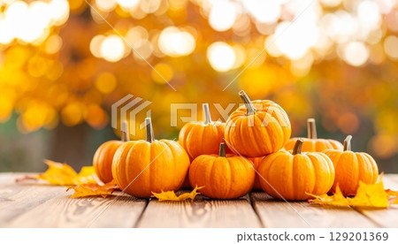 Orange pumpkins and fallen autumn leaves on a rustic wooden table capture the essence of the fall harvest season 129201369