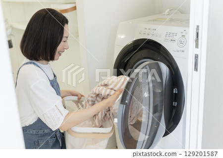 一位 50 多歲的女士正在把衣物放入洗衣機 一位 50 多歲的女士正在把衣物放入洗衣機 129201587