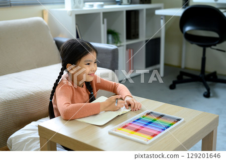 Happy child doing homework or art project sitting at wooden table with vibrant coloring pens 129201646