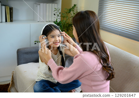 Happy asiam girl sitting on sofa listening to audio through headphones 129201647