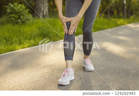 Sporty woman holding knee in pain after exercise, sports injury limiting activity, structures joint 129202985