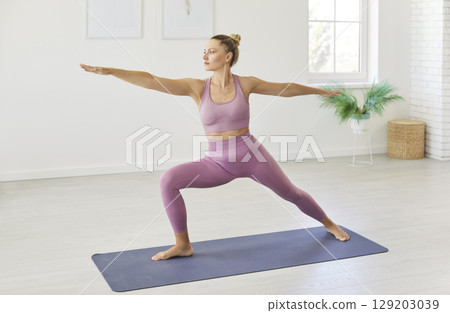 Motivated young woman doing stretching exercise on fitness karemat, keeping arms sideways Motivated young woman doing stretching exercise on fitness karemat, keeping arms sideways 129203039