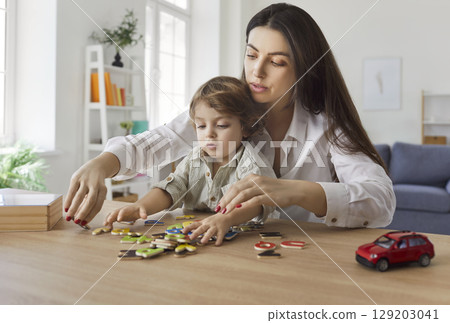 Mother and son, nanny woman, child sitting at table, playing together, engaging in puzzle game fun 129203041