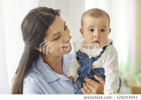 Caring brunette young mother holding baby on hands, expressing her love, smiling Caring brunette young mother holding baby on hands, expressing her love, smiling 129203042