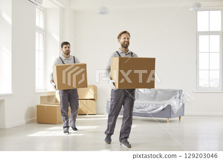 Two busy man movers carrying cardboard boxes with belongings, working in relocation service 129203046