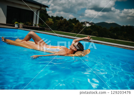 Top view of young woman in swimming pool outdoors on floating bed, relaxing. Top view of young woman in swimming pool outdoors on floating bed, relaxing. 129203476