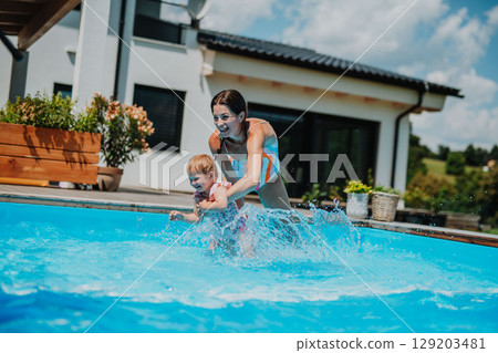 Mom playing with little daughter in backyard pool, having fun. Mom playing with little daughter in backyard pool, having fun. 129203481