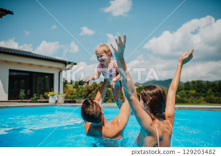 Young family with small daughter in swimming pool outdoors in backyard garden. Young family with small daughter in swimming pool outdoors in backyard garden. 129203482