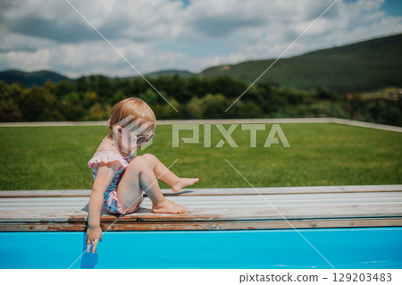 Child sitting by the poolside and playing. Child sitting by the poolside and playing. 129203483